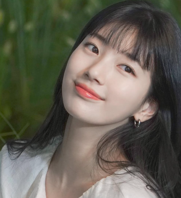 韓國女星秀智黑色齊瀏海長髮造型，展示白皙透亮肌膚與珊瑚色唇妝，呈現韓系自然裸妝護膚美感。