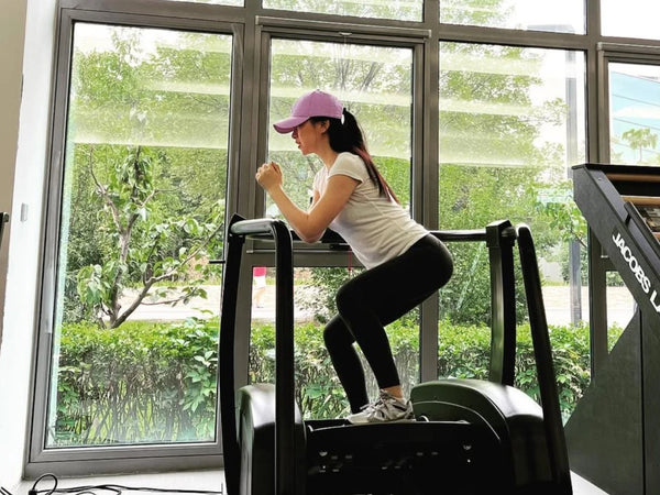 朱珠身穿白色上衣及瑜珈褲於健身室練習深蹲，示範如何透過運動維持優雅體態。