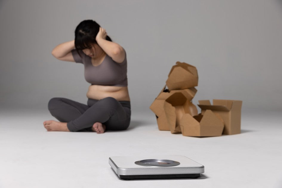 女士為體重上升及水腫肚腩感到困擾，坐在電子磅與外賣紙盒旁，呈現節後肥胖焦慮。